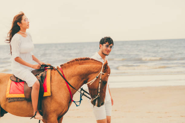 istock Young couple goes horse riding on tropical beach. 1008215414