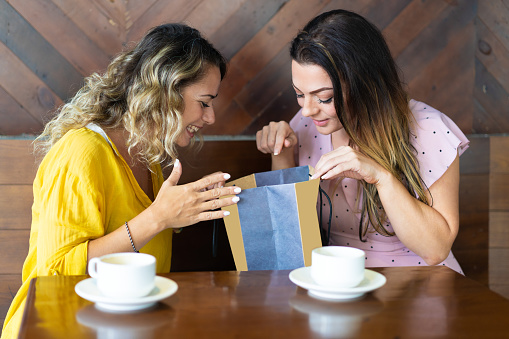 Smiling lady showing purchase to friend in cafe. Women drinking coffee and sitting at table. Women friendship and shopping concept.