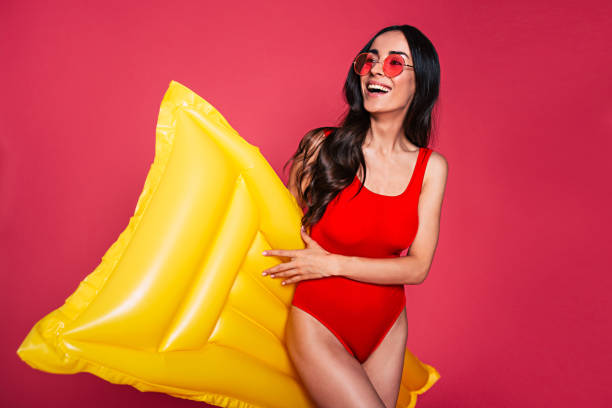 hermosa joven sonriente vestida en traje de baño rojo y vidrios con colchón inflable amarillo aislado sobre fondo rosa - swimwear bikini women fashion model fotografías e imágenes de stock