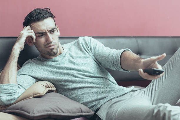 istock Dissatisfied Young Man Changing TV Channel at Home 1008243814