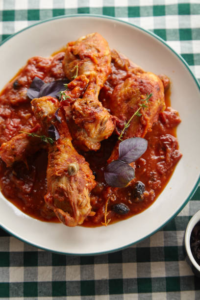 istock Chicken legs cooked in italian cacciatore style with tomato sauce and fresh basil on green checkered table-cloth 1008263644