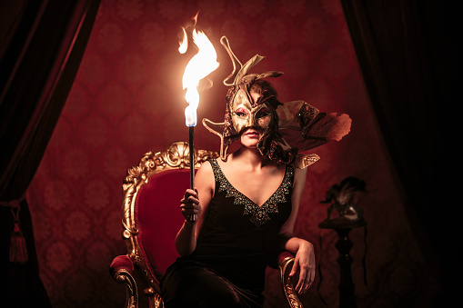 Mysterious woman wearing a venetian mask and holding fire torch
