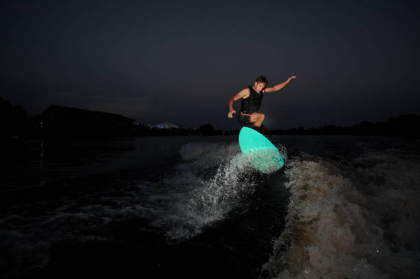 Athletic male wakesurfer riding down the river against the background of sky at summer night