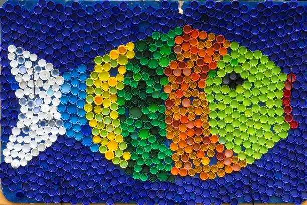 Photo of Fish mosaic deocoration made of cororful plastic bottle caps . Summer season and travel concept. Handmade crafts. Recycling art.