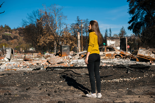 Young owner woman checking burned and ruined house and yard after fire, consequences of fire disaster accident. Ruins after fire disaster, loss and despair concept.