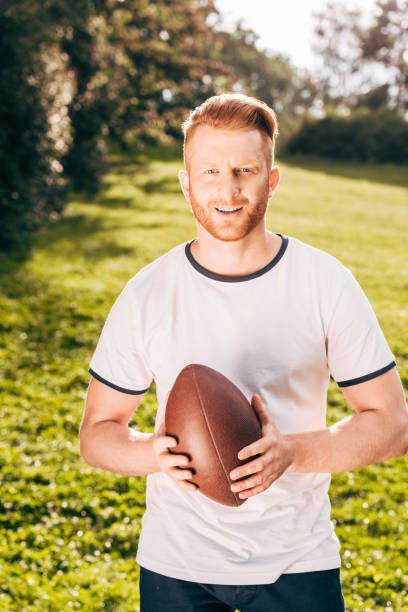 istock handsome man holding rugby ball and smiling at camera in park 1008304882