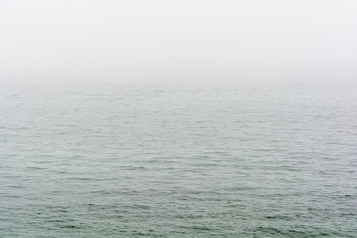 Flat grey sea with wavelets disappearing in the fog.
