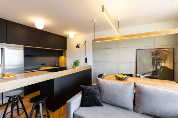istock Lights above countertop in open black kitchen interior with grey sofa and dining table. Real photo 1008307820