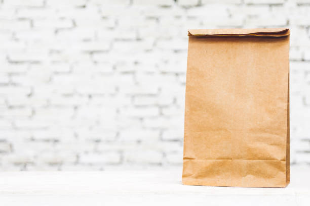 istock Blank paper bag with copy space for your brand on table against white brick wall background 1008320894