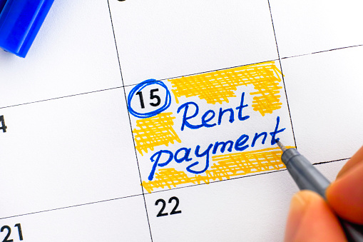 Woman fingers with pen writing reminder Rent Payment in calendar. Close-up.