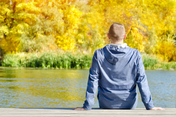 istock Young man is sitting on the dock. Autumn, sunny. Back view 1008327870