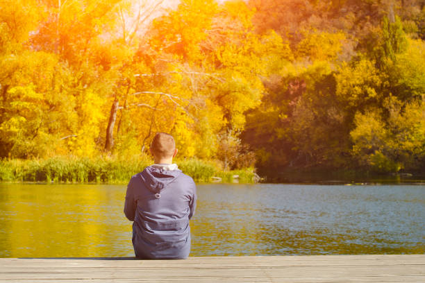 istock Young man sits on the pier. Autumn sunny day. Back view 1008328020
