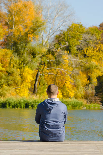 istock Young man sits on the pier. Autumn sunny day. Back view 1008328044