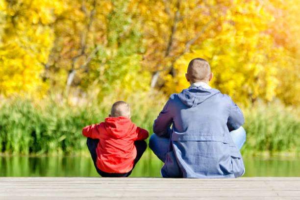 istock Father and son are sitting on the dock. Autumn, sunny. Back view 1008336354