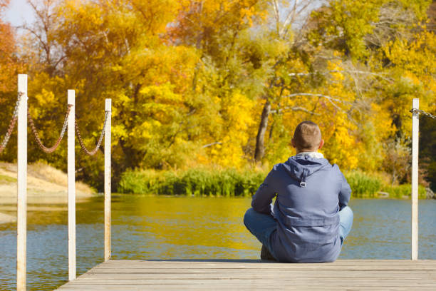 istock Young man sits on the pier. Autumn sunny day. Back view 1008336506