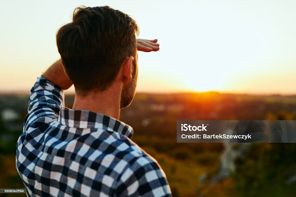 Man standing on meadow in mountains and admiring sunset Looking Stock Photo