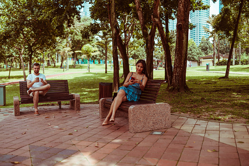 Young couple sitting on the bench and using smart phone.