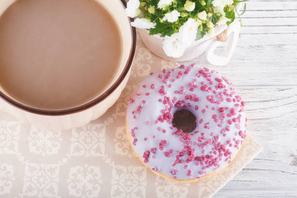 istock Three donut, a cup of coffee and flowers on a white table 1008366842