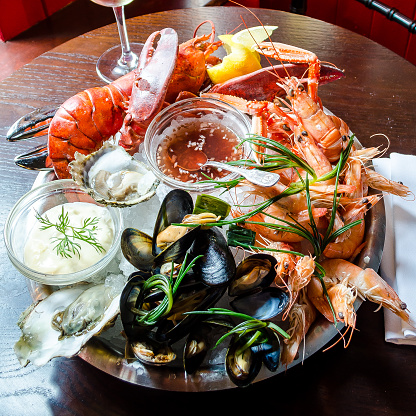 fresh seafood platter with red lobster, langoustine, prawns, mussels, oysters, clams, with a tartare and sweet chilli sauce on a wooden background