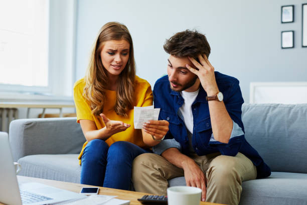 istock Experiencing financial difficulties. Worried young couple sitting on the sofa and looking at bills 1008372570
