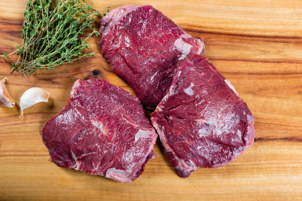 Raw beef cheeks on chopping board Raw beef cheeks on chopping board with herbs cheek stock pictures, royalty-free photos & images