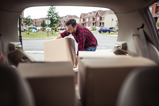 Caucasian man loading moving boxes in to his car. View from the car trunk