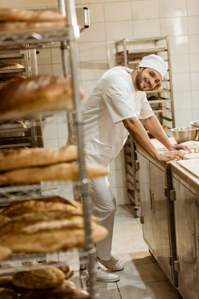 istock smiling young baker with raw dough at workplace on baking manufacture 1008379408