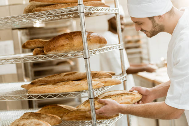 istock handsome young baker putting fresh bread loaf on shelf at baking manufacture 1008379796