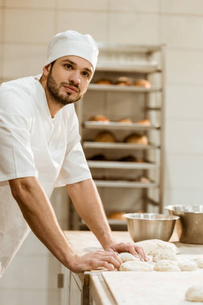 istock handsome young baker with raw dough at workplace on baking manufacture 1008380036