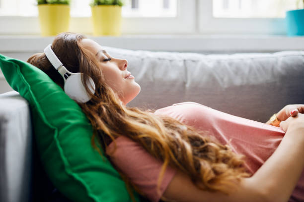 portrait of a beautiful young woman lying on sofa with headphones on and closed eyes, relaxing - ouvir musica imagens e fotografias de stock