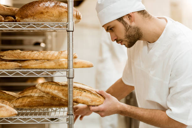 istock side view of handsome baker putting fresh bread on shelf at baking manufacture 1008382748