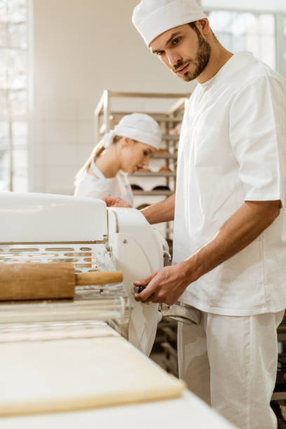 istock handsome baker working with industrial dough roller at baking manufacture 1008383072