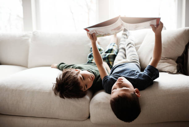 Shot of two adorable brothers reading books while relaxing together on the sofa at home