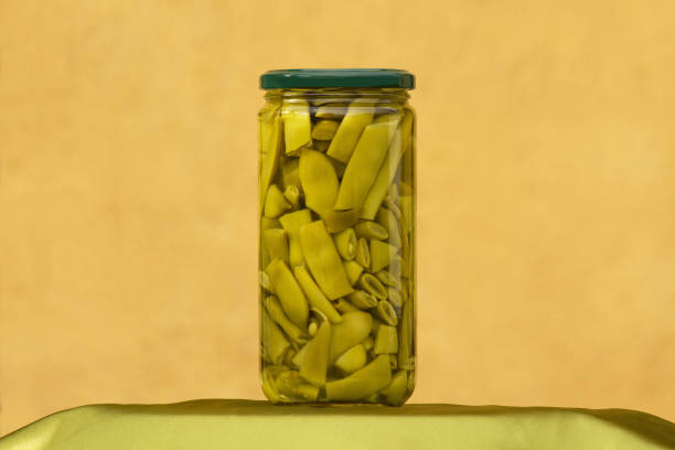 Jar or glass container showing green canned beans with ocher wall background - Jar or glass container showing canned green beans with ochre wall background