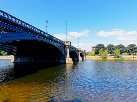 The three arch road bridge, Trent Bridge, spans the River Trent on a hot, bright summer day.
