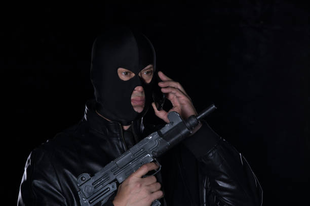 istock a man in a mask and with a gun and with a phone 1008406238