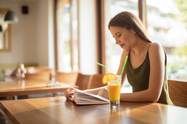 istock Young woman reading book and drinking juice in restaurant 1008408376