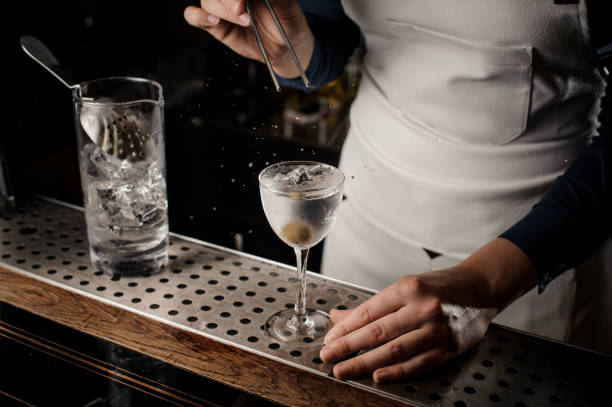 istock Female bartender throwing into the transparent cocktail one olive with tweezers 1008408400