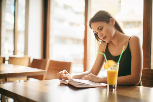 istock Young woman reading book and drinking juice in restaurant 1008408442