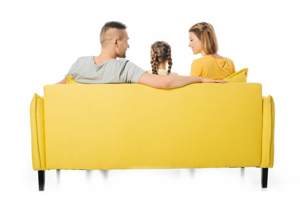 vista posteriore di genitori e figlia seduti su divano giallo isolato su bianco - rear view family isolated child foto e immagini stock