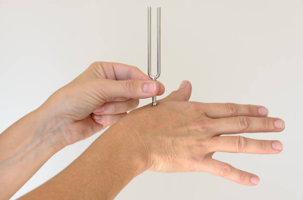 Anonymous person holding metal tuning fork against hand for therapy over white background. Includes copy space.