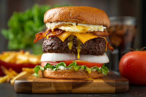 A bacon cheeseburger with fried egg, and all the trimmings. Commercial lighting.