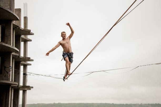 Fearless man balancing on a slackline high against empty building and sky Fearless man balancing on a slackline high against empty building and sky on rainy summer day highlining stock pictures, royalty-free photos & images