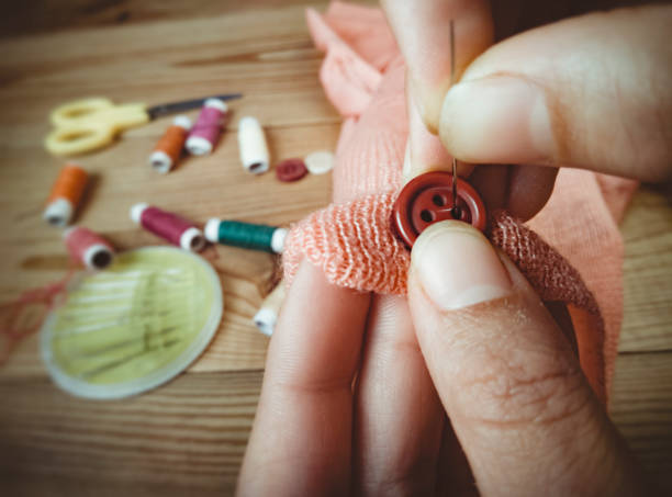 Indoor close-up of woman hands stitch button and other haberdashery pleased on wooden table.