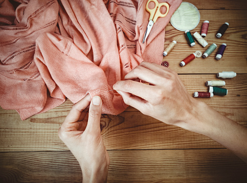 Indoor close-up of woman hands stitch cloths and other haberdashery pleased on wooden table.