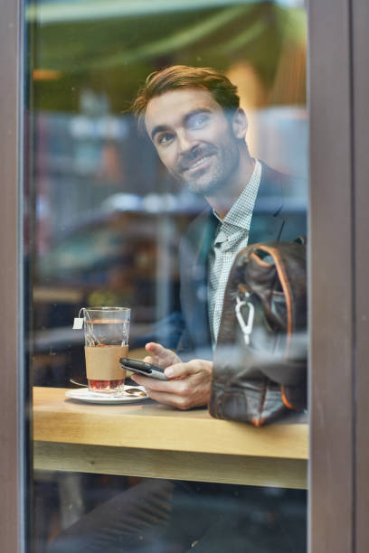istock Smiling businessman with mobile phone seen through glass 1008455302