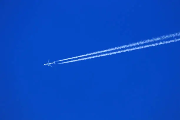 Airplane with two  chemtrails or condensate trace with blue sky, high in the air