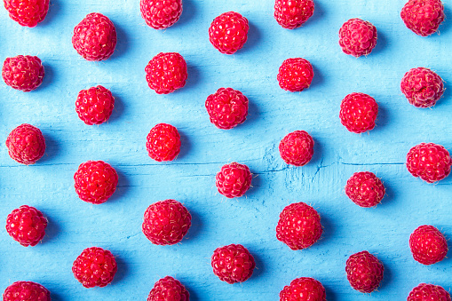 Many fresh raspberries on blue wooden background. Bright texture for design. Top view.