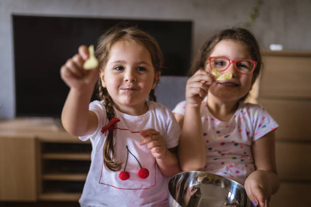 Playful children having fun while eating snacks Cute and lovely young sisters, sitting at home, eating some snacks. family eating potato chips stock pictures, royalty-free photos & images