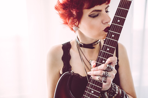 Young woman dressed in rock and heavy metal style, kissing an electric guitar.